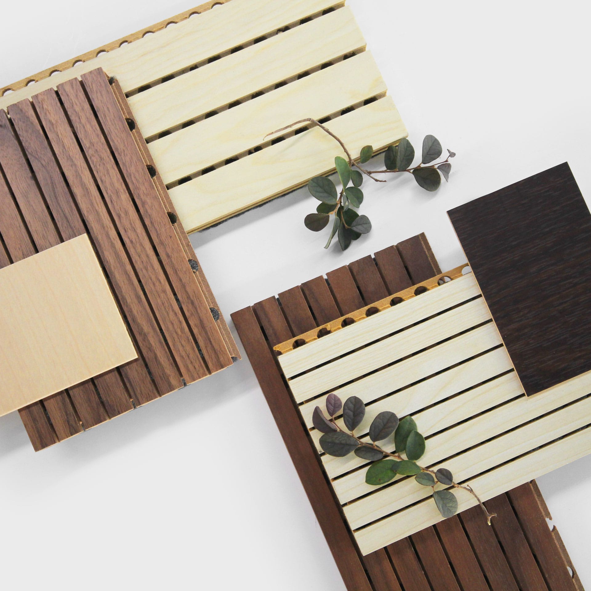 Wood samples in various shades of brown and beige, showcasing Fire-Safe Timber Cladding That Doesn’t Sacrifice Craft, are arranged on slatted wooden boards with eucalyptus branches, set against a white background.