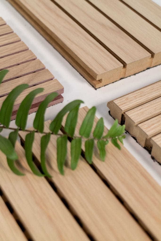 Close-up of several fire-safe timber cladding panels arranged on a white surface, with a green leafy branch placed diagonally across the foreground, highlighting woodwork that doesn’t sacrifice craft.