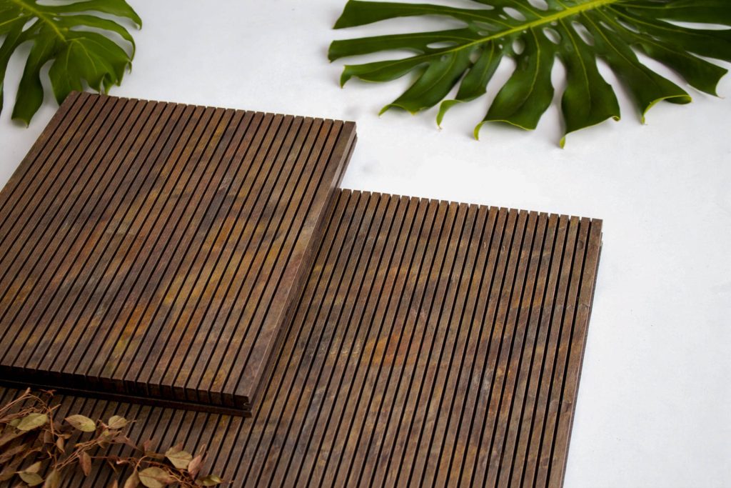Two rectangular, dark wooden slatted panels placed on a white surface, decorated with two large green tropical leaves and some dried brown leaves.