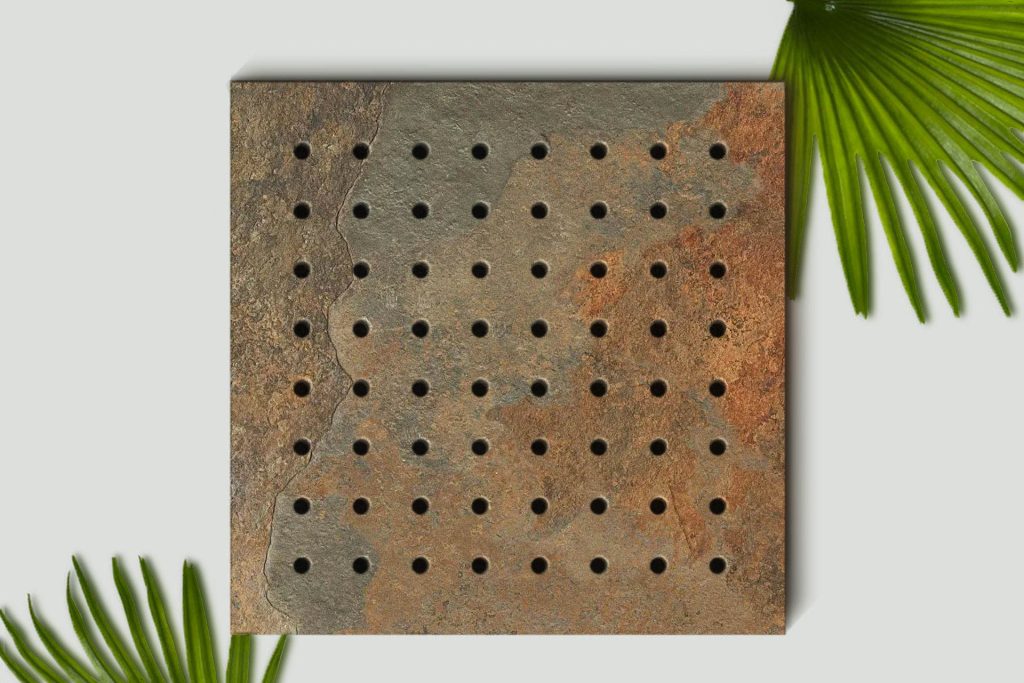 A square, textured, brown stone with a grid of round holes sits on a white surface, flanked by green palm leaves in the corners.