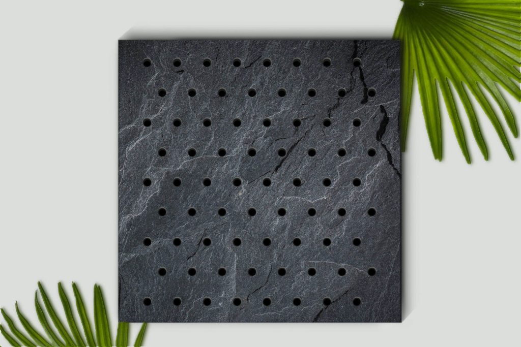 A square black slate with a grid of small round holes sits on a light background, bordered by green palm leaves in the top right and bottom left corners.