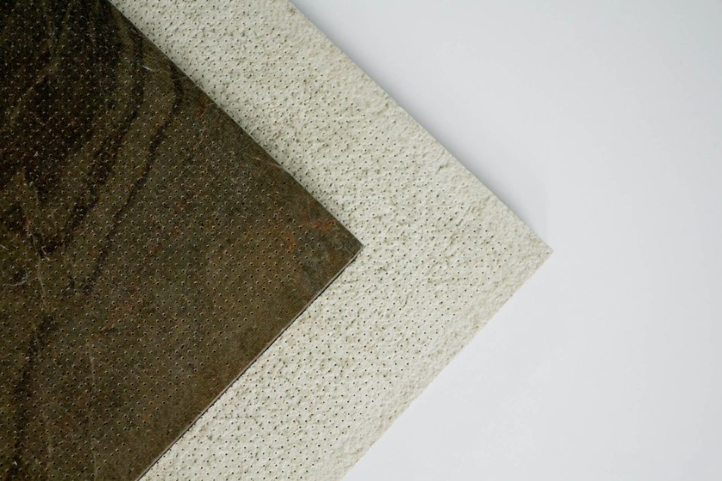 Two textured rectangular panels overlap on a white background; one panel is dark brown and positioned above a larger, light beige panel. Both panels have a dotted, speckled surface pattern.