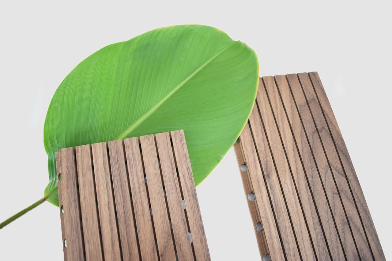 A large green leaf is placed behind two Timberix Grooved Acoustic Panels, each featuring vertical grooves, all set against a plain light background.